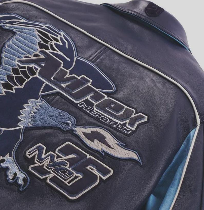 K&ouml;nnte beinhalten: Marineblaue Lederjacke mit gesticktem Adler und Textdetails. Die Jacke hat ein gro&szlig;es Adlerdesign in Blau- und Wei&szlig;t&ouml;nen sowie den Text "Apex Nitroforum" und die Zahl "35". Wei&szlig;e und hellblaue Akzente sind sichtbar.