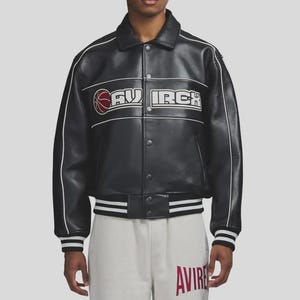 Puede incluir: Chaqueta de cuero negra con ribetes blancos y la palabra "AVIRE" en blanco y rojo. La chaqueta presenta un gr&aacute;fico de baloncesto y la palabra "AVIRCH" en blanco. La chaqueta tiene cierre de botones y pu&ntilde;os a rayas.