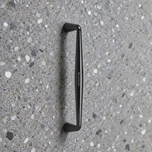 May include: A matte black cabinet pull handle with a smooth, elongated, and slightly curved design. The handle features a subtle, vertically oriented brand engraving on its front surface, showcasing a clean and functional aesthetic.