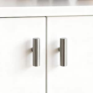 Könnte beinhalten: Zwei Schrankgriffe aus gebürstetem Nickel mit vertikalen Rillen sind an einer weißen Schranktür angebracht. Die zylindrischen Griffe haben ein modernes Design und sind gleichmäßig angeordnet. Der Schrank ist Teil eines Küchen- oder Badezimmerset.