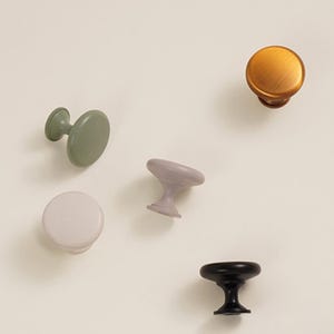 Pu&ograve; includere: Un assortimento di pomelli per mobili in vari colori, tra cui verde salvia, lavanda, bronzo, bianco sporco e nero. I pomelli hanno forme e stili diversi, adatti a progetti di arredamento o decorazione d'interni.