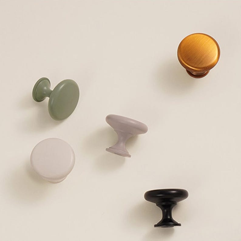 Pu&ograve; includere: Un assortimento di pomelli per mobili in vari colori, tra cui verde salvia, lavanda, bronzo, bianco sporco e nero. I pomelli hanno forme e stili diversi, adatti a progetti di arredamento o decorazione d'interni.