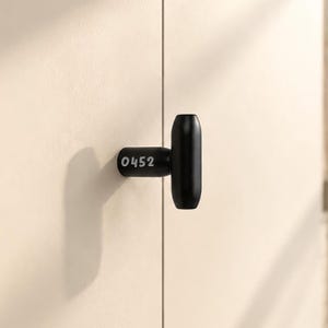 Könnte beinhalten: Ein mattschwarzer, T-förmiger Schrankknopf, der auf einer hellen Oberfläche montiert ist. Der zylindrische Sockel des Knopfes trägt die weiß aufgedruckte Nummer 0452. Der Griff hat ein glattes, abgerundetes und längliches Design.