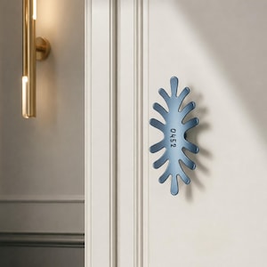 May include: A blue door handle with an organic, multi-pronged shape resembling a stylized leaf or coral. The handle is mounted on a white door and features the number 0452 embossed vertically in the center of its smooth, matte surface.