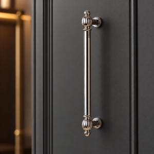 May include: A polished silver-tone metal cabinet handle featuring a long, smooth cylindrical bar with decorative, vertically ribbed spherical finials at both ends. The handle is mounted vertically on a dark gray paneled cabinet door.