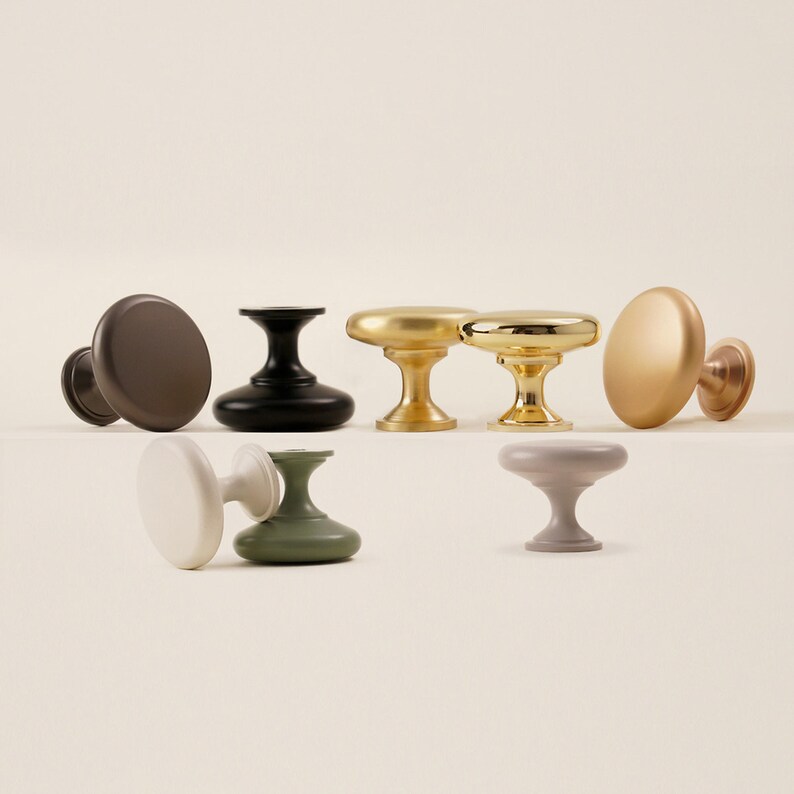 Pu&ograve; includere: Una collezione di pomelli per mobili in vari colori e finiture. I pomelli includono marrone opaco, nero, oro e tonalit&agrave; tenui di bianco, verde e grigio. Ogni pomello ha una testa rotonda o ovale e una base a piedistallo.