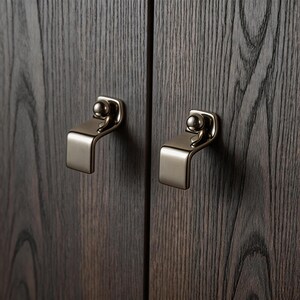 Peut inclure: Gros plan sur deux poignées de meubles en nickel brossé montées sur des portes d'armoires en bois foncé. Chaque poignée comporte une poignée incurvée et un petit bouton sphérique. Le grain du bois est visible.