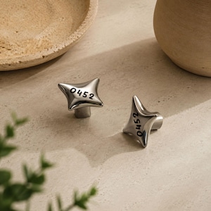 May include: Two silver-toned metal cabinet knobs with a four-pointed star shape. Each knob features the black printed number 0452 on its front surface. The knobs have a smooth, reflective finish and a cylindrical base for mounting to furniture.
