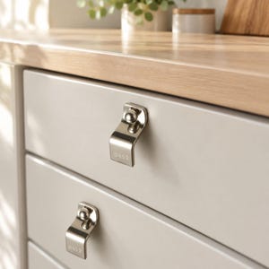 May include: Two polished silver-toned metal drawer pulls with a curved, angular design attached to light grey cabinet drawers. Each pull features a small spherical accent at the top and the engraved number 0452 on the lower front surface.