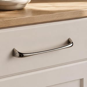 May include: A polished chrome cabinet pull with a curved, slender design attached to a white drawer front. The left mounting base features the engraved text 0-451, showing a metallic finish that reflects light across its smooth, contoured surface.