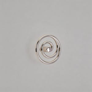 Puede incluir: Un pomo de armario plateado pulido con un diseño en espiral. El pomo tiene forma circular con un poste central para el montaje. El herraje está diseñado para su uso en cajones y armarios.