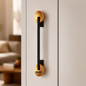 May include: A vertical cabinet handle featuring a matte black rectangular bar connected to two circular gold-toned end caps. The bottom gold cap is engraved with the black numerical text 0452. The hardware is mounted on a light-coloured door panel.
