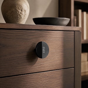 May include: A dark brown wooden drawer featuring a circular black knob. The knob is divided into two halves, with the left side solid black and the right side featuring the white numerical text 0452 printed vertically on its surface.
