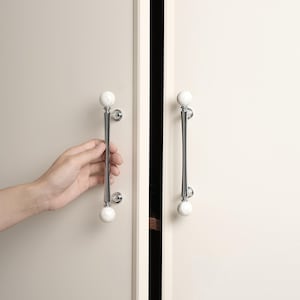 May include: Cabinet door handles with a polished chrome finish and white, marble-effect spheres. The handles are mounted on a light-coloured cabinet door. Each handle is approximately 20 cm in length.