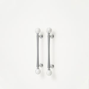 May include: A pair of polished chrome door handles featuring white marble sphere details. The handles have a slender, elongated form with a flared central section. Marble spheres are positioned at the top and bottom of each handle, enhancing the design.