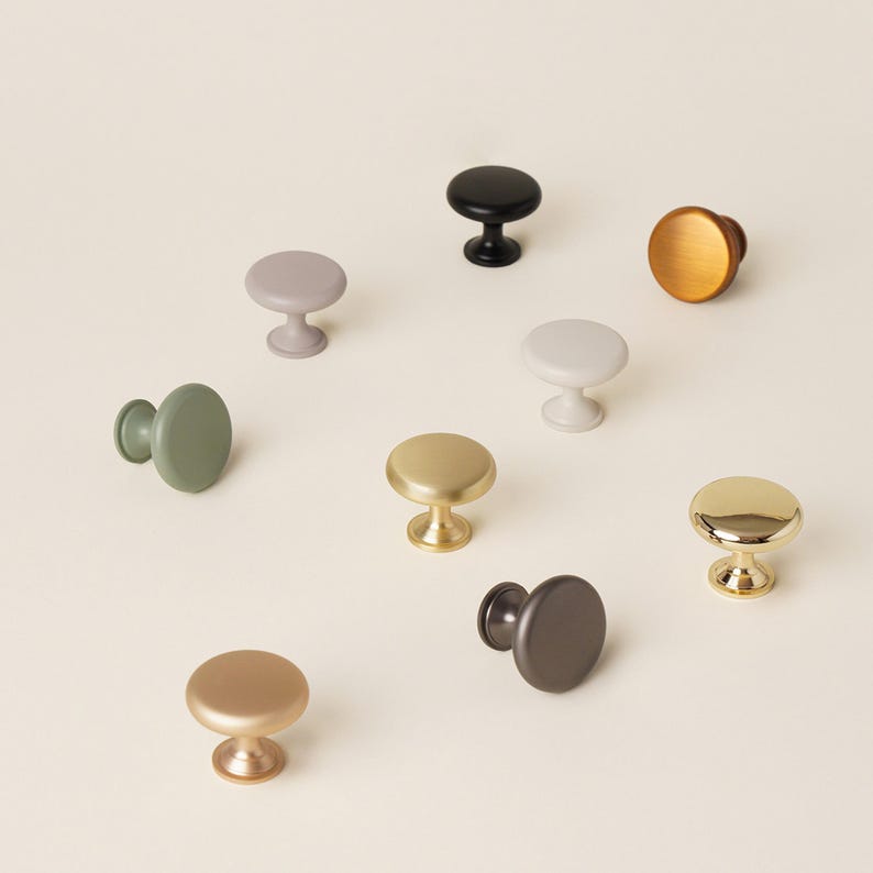 Pu&ograve; includere: Una collezione di pomelli per mobili in vari colori, tra cui oro, nero e verde. I pomelli hanno un design rotondo a forma di fungo e sono realizzati in metallo. I pomelli sono disposti su una superficie di colore chiaro.