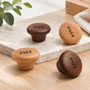 May include: Four round wooden cabinet knobs in two different wood tones, light and dark brown. Each knob features a smooth, rounded top surface with the number 0452 clearly printed in a dark, sans-serif font on the face of the wood grain.