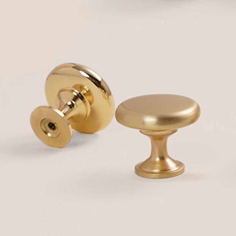 Pu&ograve; includere: Due pomelli dorati per mobili. Uno &egrave; appoggiato su un lato, rivelando l'attacco a vite. L'altro &egrave; in posizione verticale, mostrando la parte superiore arrotondata e la base a piedistallo. I pomelli hanno una finitura liscia e opaca, progettati per mobili.