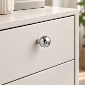 May include: A spherical, polished chrome cabinet knob with a reflective metallic surface. The knob features the engraved numbers 0452 on its front face and is mounted on a smooth, off-white drawer front of a piece of furniture.