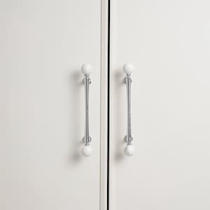 May include: Two white cabinet doors with matching handles. Each door has a polished chrome handle with a white, marble-effect sphere at each end. The handles are vertically aligned, adding elegance to the minimalist design.