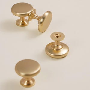 Pu&ograve; includere: Quattro pomelli dorati per mobili con finitura opaca sono disposti su uno sfondo chiaro. I pomelli hanno una parte superiore rotonda e piatta e una base decorativa. L'hardware &egrave; progettato per mobili e decorazioni per la casa.