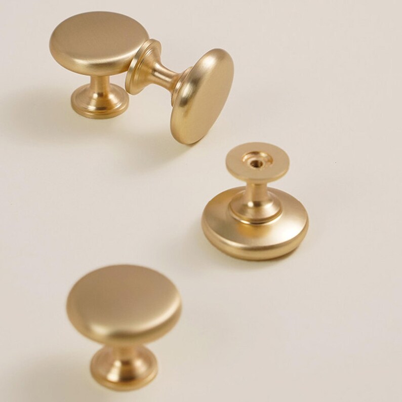 Pu&ograve; includere: Quattro pomelli dorati per mobili con finitura opaca sono disposti su uno sfondo chiaro. I pomelli hanno una parte superiore rotonda e piatta e una base decorativa. L'hardware &egrave; progettato per mobili e decorazioni per la casa.