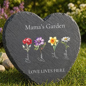 May include: Heart-shaped black slate garden stone with the text "Mama's Garden" and "LOVE LIVES HERE". It features watercolor illustrations of four flowers with names: Olivia, Emma, John, and William. The stone is set in a grassy garden.