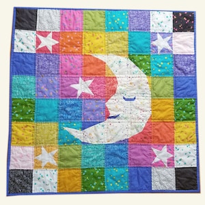 May include: A colourful patchwork quilt with a white crescent moon and stars appliqued on top. The quilt is made of various fabrics in shades of pink, blue, green, yellow, and orange.