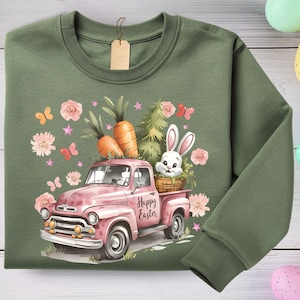 May include: Olive green sweatshirt featuring a pink vintage truck carrying carrots, a bunny, and flowers. The truck has the words "Happy Easter" on the side. Butterflies and stars are also part of the design.
