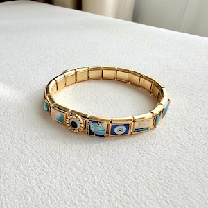 May include: Gold-toned bracelet with rectangular links and colorful enamel charms. Charms feature blue and white designs, including an eye, clouds, and a boat. A turquoise stone accents the bracelet's clasp.
