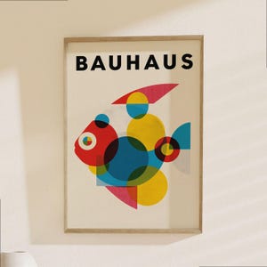 Könnte beinhalten: Gerahmter Bauhaus-Kunstdruck mit einem farbenfrohen geometrischen Fischdesign. Der Fisch besteht aus sich überlappenden Formen in Rot, Gelb, Blau und Rosa. Das Wort "BAUHAUS" ist in schwarzen Blockbuchstaben oben auf dem Druck abgebildet.