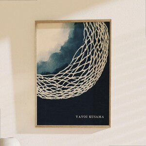 May include: Framed art print featuring a white net-like design over a dark blue and light blue watercolor background. The artwork is signed "YAYOI KUSAMA" in white text at the bottom. The frame is made of light-colored wood.