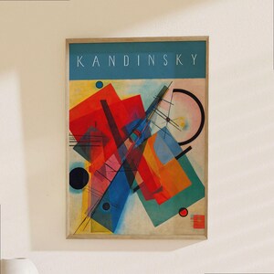 Op de afbeelding: Een ingelijste kunstdruk met een abstracte Kandinsky-compositie met geometrische vormen in rood, blauw, geel en oranje. Het bovenste gedeelte heeft een blauwgroene band met de witte tekst KANDINSKY. De print zit in een lichthouten lijst.