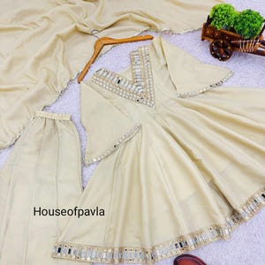 Könnte beinhalten: Cremefarbenes indisches Anzug-Set mit Palazzo-Hose, einem langen Oberteil mit Spiegelverzierungen und einem passenden Dupatta. Das Set enthält braune Sandalen mit silbernen Akzenten. Der Text "Houseofpavla" ist sichtbar.