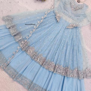 May include: A pale blue formal dress with silver detailing. The dress has a layered skirt, long sleeves, and detailed silver embroidery. The text "HouseOfPavla" is visible on the dress.