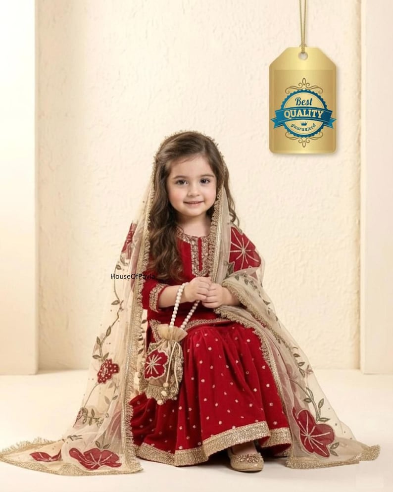 May include: A young girl in a red velvet outfit with gold trim and a matching head covering. The outfit includes a long-sleeved top and a flared skirt. A small beaded purse and a tag that says "Best Quality Guaranteed" are also visible.