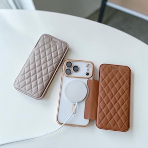 Pode incluir: Duas capas retangulares para telemóvel com padrão de diamante acolchoado e um smartphone central com moldura em ouro rosa. Uma capa é cinza-acastanhado e a outra é castanho-claro. O smartphone está ligado a um carregador magnético sem fios.