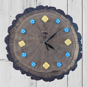 May include: A handcrafted wooden clock made from a cross-section of a tree trunk. The clock face features a natural wood grain pattern, with black clock hands and yellow and blue accents. The clock measures approximately 12 inches in diameter.