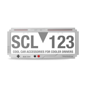 May include: A rectangular, silver-colored car license plate with the text "SCL 123" in large, gray letters. Below, the text reads "COOL CAR ACCESSORIES FOR COOLER DRIVERS". The design includes a controller-style button layout.
