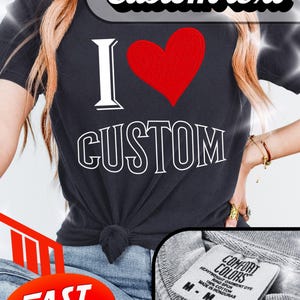Può includere: T-shirt nero con la scritta "I ❤️ CUSTOM" in bianco e un cuore rosso. La maglietta ha un nodo sul davanti e un'etichetta "COMFORT COLORS". Un adesivo ovale rosso dice "FAST DELIVERY".