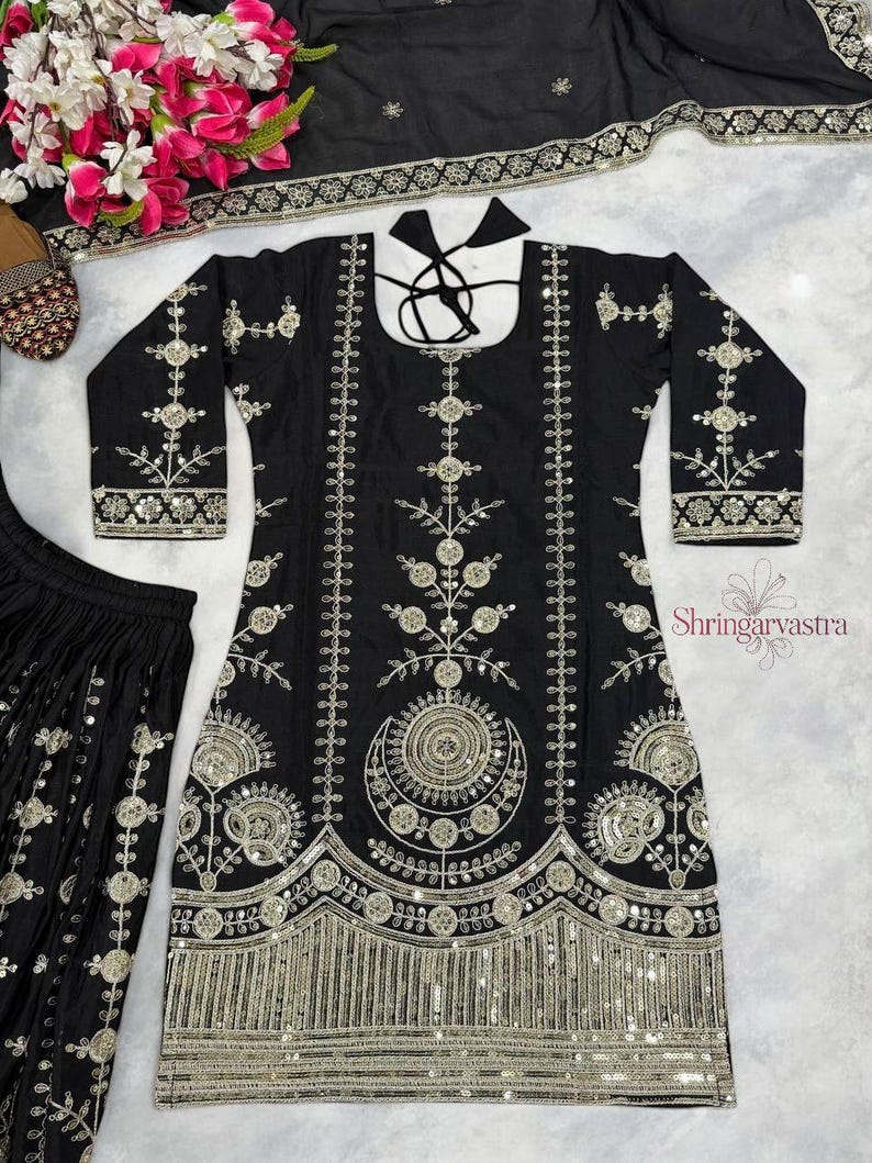 May include: Black embroidered tunic and matching pants set with silver embellishments. The tunic features intricate floral and geometric patterns, long sleeves, and a decorative neckline. The set includes a matching scarf and is suitable for special occasions.