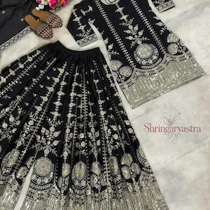 May include: A black embroidered three-piece outfit with a matching top, wide-leg pants, and a scarf. The set features intricate silver embroidery and embellishments. A pair of embellished sandals and a bouquet of flowers are also present.