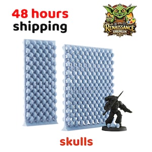 Könnte beinhalten: Zwei hellblaue, schädelartige Formen und eine schwarze Miniaturfigur stehen auf weißem Hintergrund. Das Wort "skulls" ist orange geschrieben. Das Renaissance Gremlin-Logo befindet sich oben rechts.