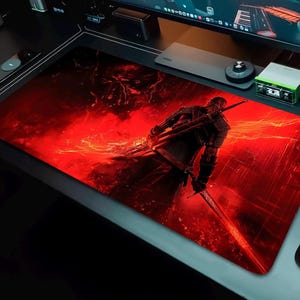 May include: Large rectangular gaming mouse pad featuring a warrior figure with two swords, set against a fiery red background. The design includes a detailed illustration of the character and a dynamic, action-oriented scene.