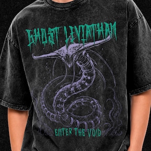 May include: A black acid-wash t-shirt featuring a graphic of a multi-eyed, serpentine creature in purple. The text "GHOST LEVIATHAN" appears in teal above the creature, and the text "ENTER THE VOID" is printed in teal below the creature.