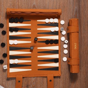 May include: A brown backgammon set with black and white game pieces, dice, and a rolled-up carrying case. The backgammon board is open, displaying the playing surface with black and white triangles. The carrying case has the number "1996" printed on it.