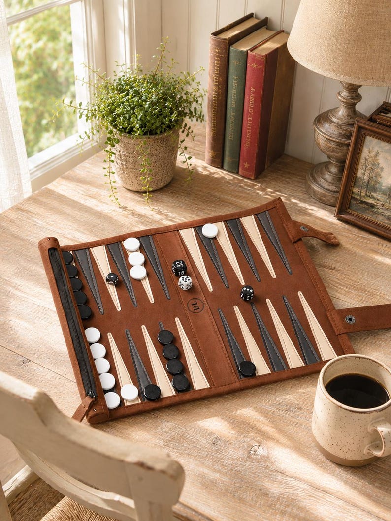 May include: A brown leather backgammon set with black, white, and grey game pieces. The board is open, with dice scattered across the playing surface. A cup of coffee and a small potted plant are also visible.