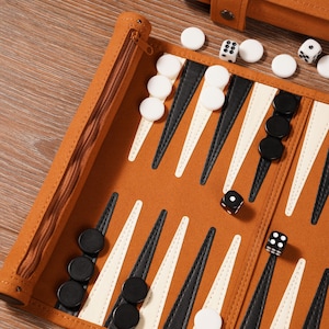 May include: A brown backgammon set with white and black game pieces. The board is open, showing the playing surface with black and white triangles. Dice and a zippered case are also visible. The set is on a wooden surface.