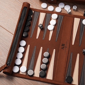 A detailed view of the leather travel backgammon board with black and white checkers in play. Custom initials are engraved on the centre panel, showcasing personalisation options on the roll-up design.