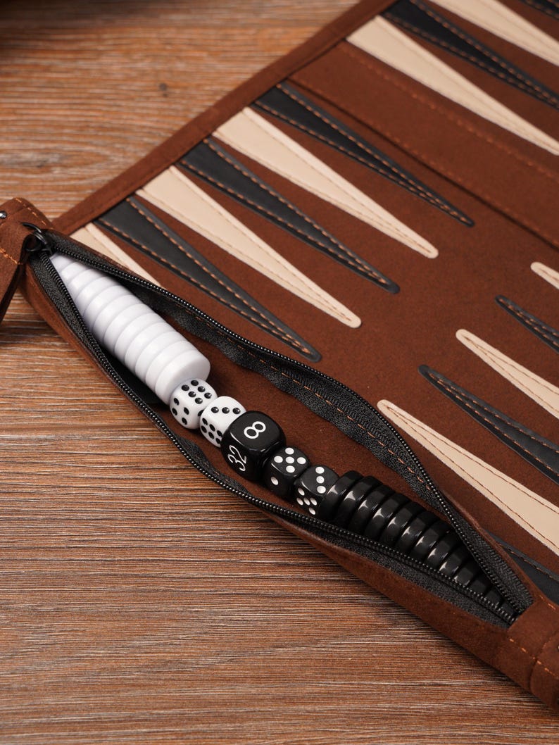 Close-up of the zippered storage pocket on a leather roll-up travel backgammon board, neatly holding black and white checkers and dice. The image highlights the compact, portable design and organized interior ideal for travel use.